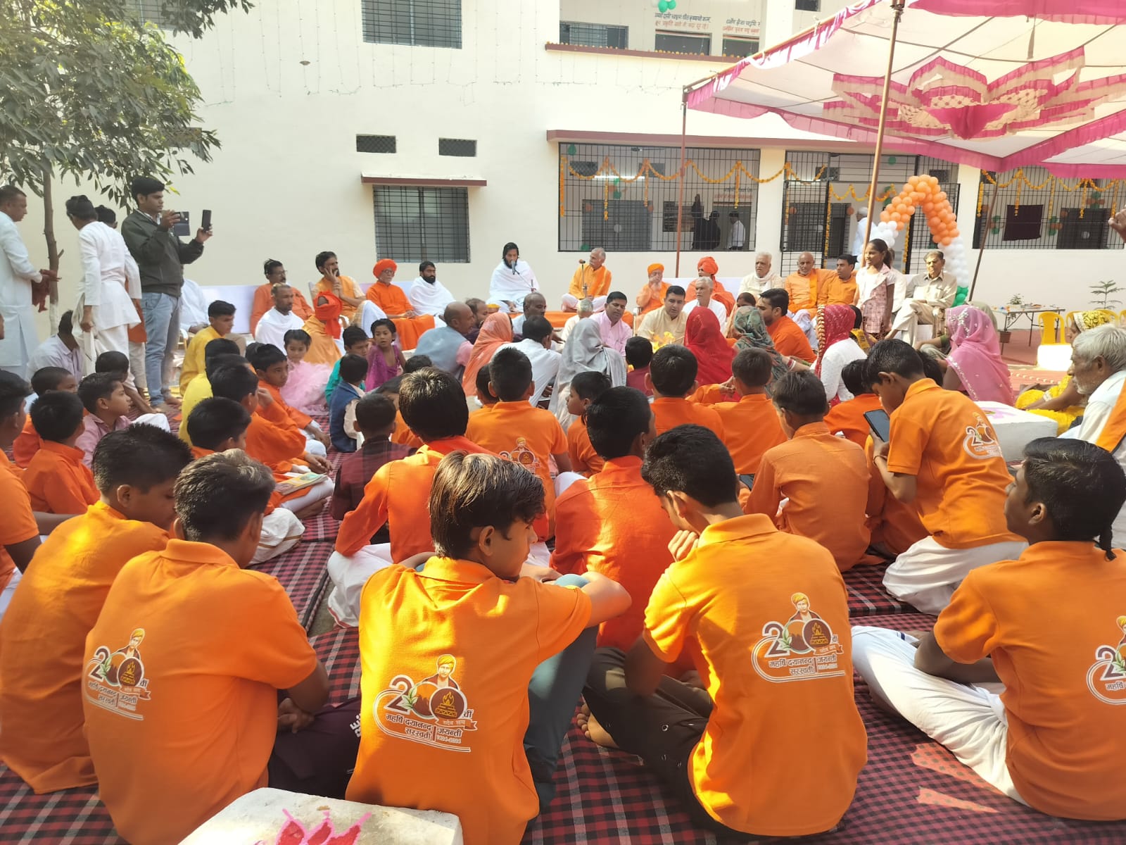 Large community gathering with students and officials under outdoor tent